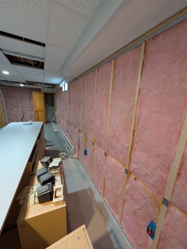 Basement under renovation with exposed pink insulation and ceiling tiles removed.