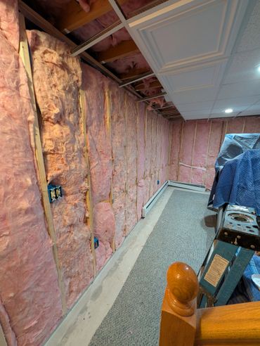 Basement wall with exposed pink insulation and drop ceiling panels partially installed.