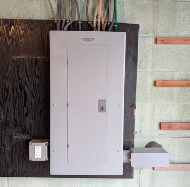 Electrical panel mounted on a wooden board with conduit wires.
