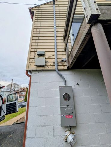 Electrical and utility boxes mounted on a house exterior wall with wooden balcony above.