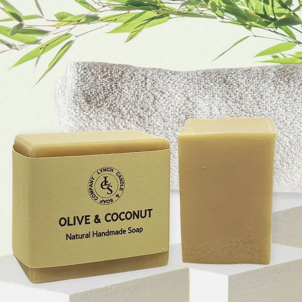 Olive and Coconut handmade soap with linen soap wrapped and bath brush and towel in the background.