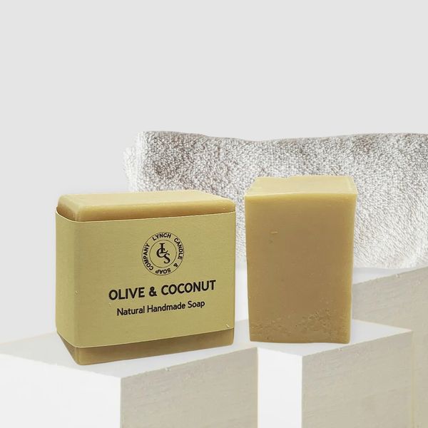Olive and Coconut handmade soap with linen soap wrapped and bath brush and towel in the background.