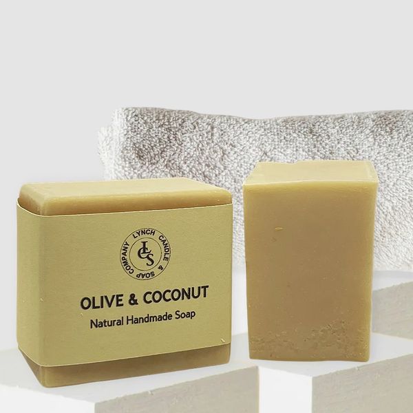 Olive and Coconut handmade soap with linen soap wrapped and bath brush and towel in the background.