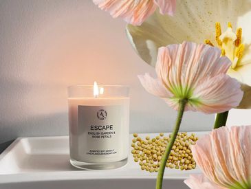 Lit scented candle with flowers in a soft, elegant setting.