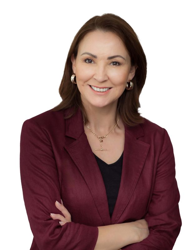Confident woman in a burgundy blazer smiling with arms crossed.