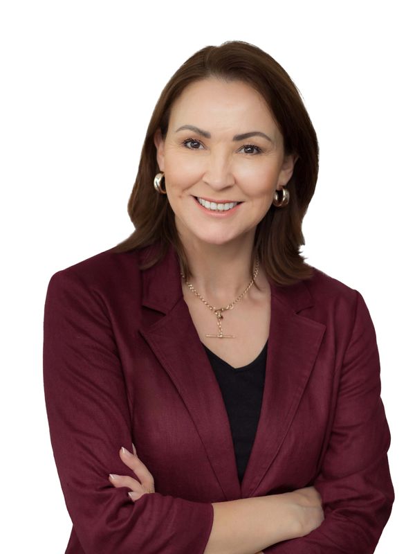 Confident woman in a burgundy blazer smiling with arms crossed.
