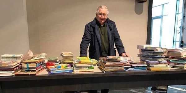 A man stands at a table with donated books all around him.