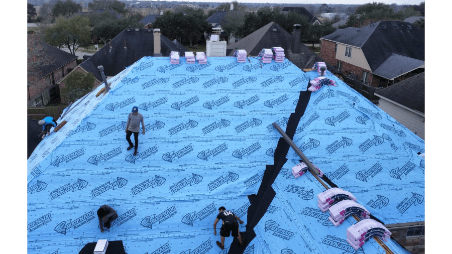 Crew installing underlayment across a large roof section