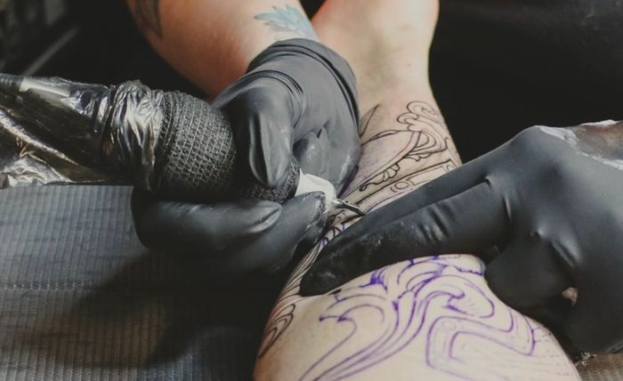 Artist working on a detailed leg tattoo
