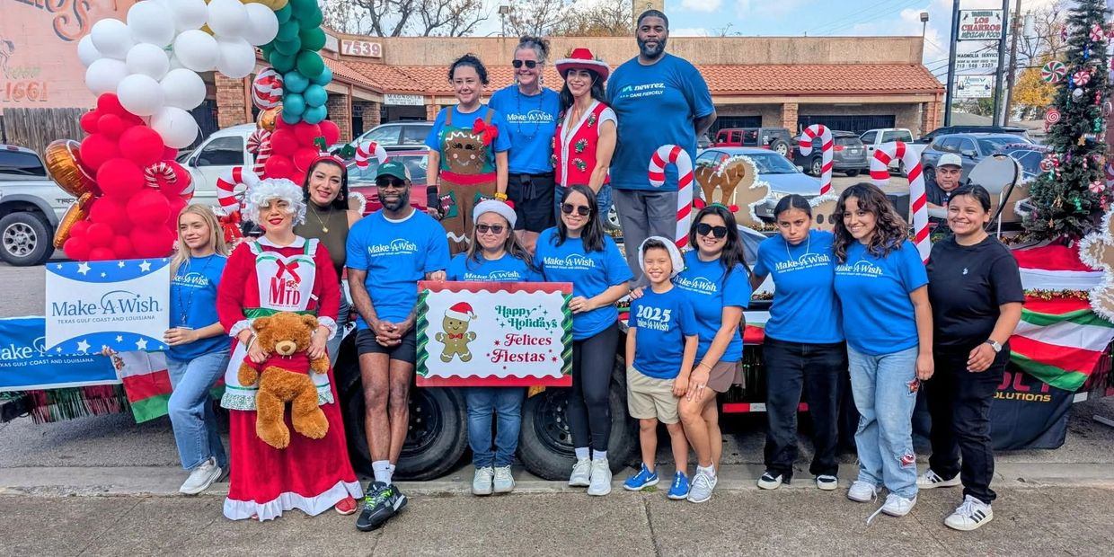 Group of people in festive attire posing with holiday decorations and Make-A-Wish signs.