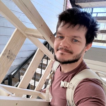 Man with backpack smiling on wooden staircase outdoors.