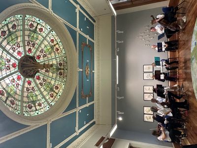 Orchestra rehearsing under a stained glass dome in an elegant room.