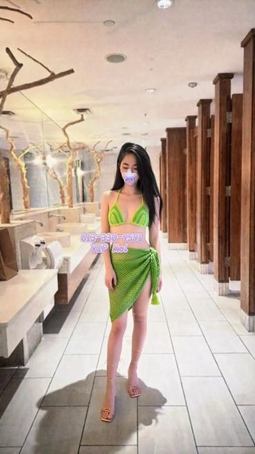 Woman in green bikini and sarong posing in stylish restroom with wooden stalls.