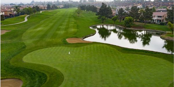A golf course with a green, sand bunkers, and a water hazard near residential houses.