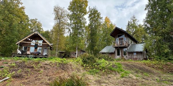 Two rustic wooden cabins surrounded by trees under a cloudy sky.