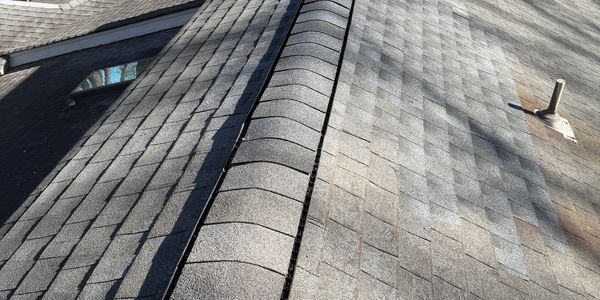 Shingled house roof with ridge vent and nearby homes in background.