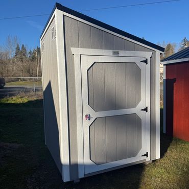 Small gray and white storage shed with a sloped roof.
