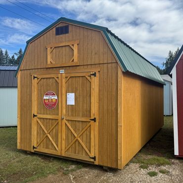 A wooden barn-style shed with double doors and a green metal roof.