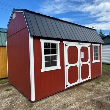 Red storage shed with white trim and double doors under a blue sky.