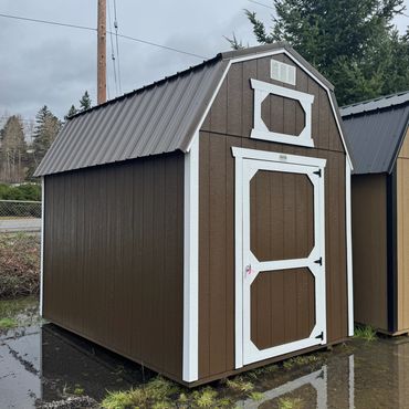 A small brown and white wooden storage shed with a sloped metal roof.