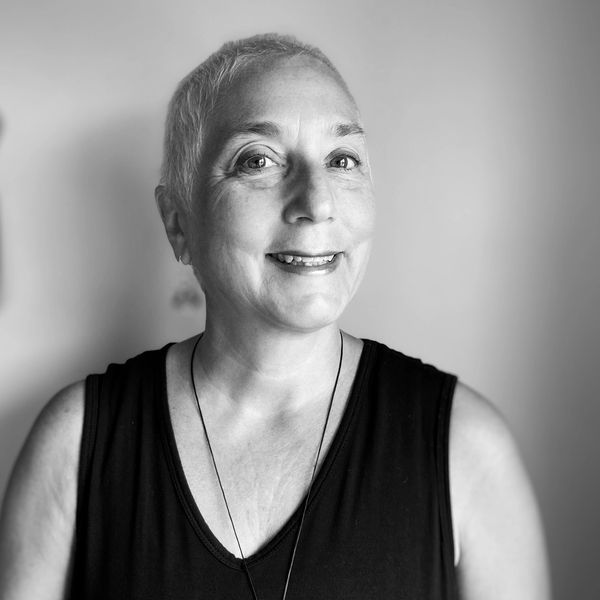 Smiling woman with short hair wearing a black sleeveless top and a pendant necklace.