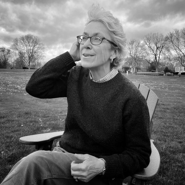 An elderly person sits outside on a chair, smiling and looking into the distance.