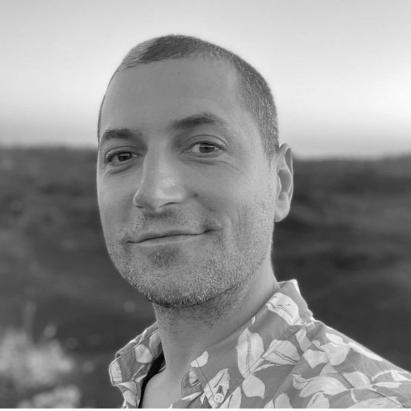 A man with a slight smile wearing a floral shirt during sunset.