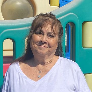 Smiling woman outside near colorful playground equipment.