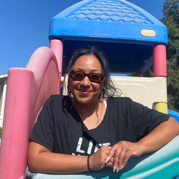 Woman wearing sunglasses at a colorful playground slide.