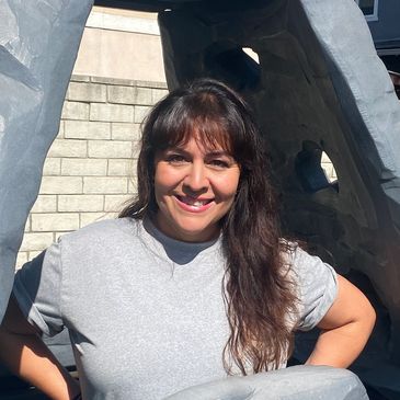 Smiling woman posing outdoors near a stone sculpture.