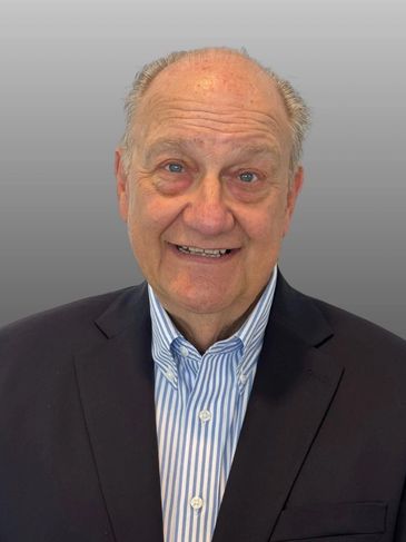 Elderly man smiling in a suit jacket and striped shirt.
