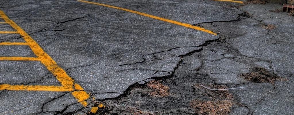 Cracked and damaged asphalt parking lot with faded yellow lines.