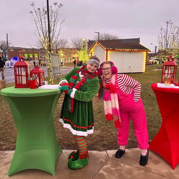 Two women in festive holiday costumes smiling and leaning together outdoors.
