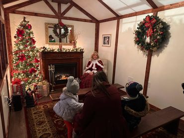 Cozy Christmas room with decorated tree, fireplace, and a woman in festive attire smiling at children.