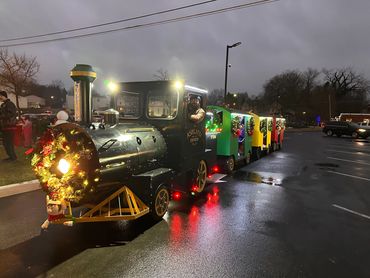 Festively decorated miniature train with colorful cars and wreaths at night.
