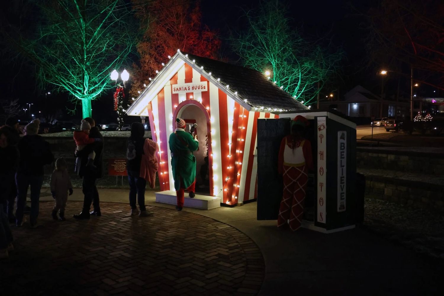 People gather around a brightly lit Santa's House at night.