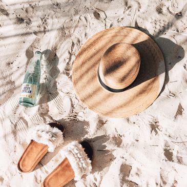 A sunhat, sandals, and a refreshing drink on sandy beach.
