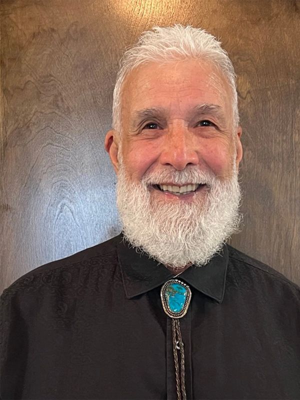 Smiling elderly man with white beard and turquoise bolo tie.