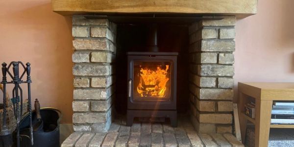 Fire burning in a wood stove inside a stone fireplace.