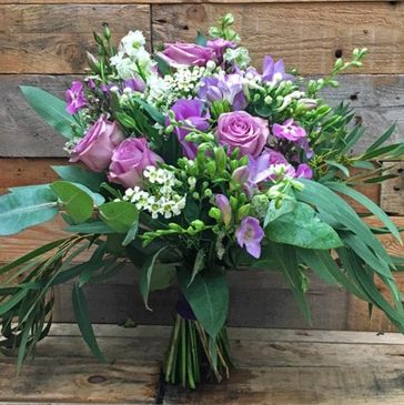 A bouquet of purple roses and white flowers with green leaves.