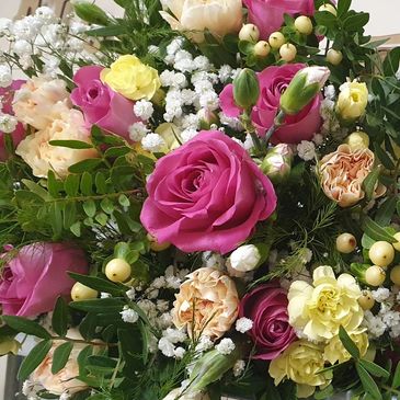 A vibrant bouquet of pink, yellow, and cream roses with greenery and white filler flowers.
