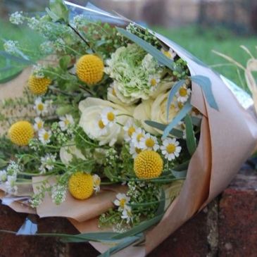 A bouquet with yellow billy balls and white flowers wrapped in brown paper.