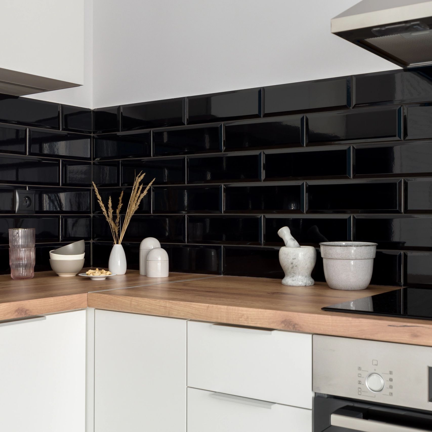 Stylish decoration on wooden countertops in small kitchen with black wall tiles.
