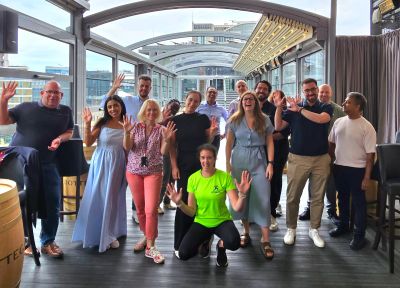 A group of people smiling and waving indoors.