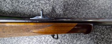 Close-up of a rifle with wooden stock and bolt action.