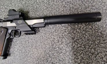 A handgun with a suppressor and red dot sight on a gray surface.