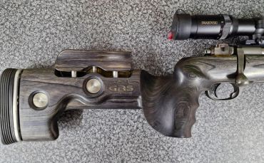 Close-up of a wooden rifle stock with ergonomic grip and scope.