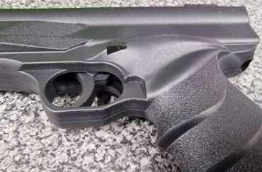 Close-up of a black firearm grip and trigger on a textured surface.