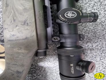 Close-up of a rifle scope mounted on a camouflaged rifle stock.
