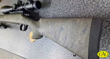 Rifle with scope on a speckled surface.